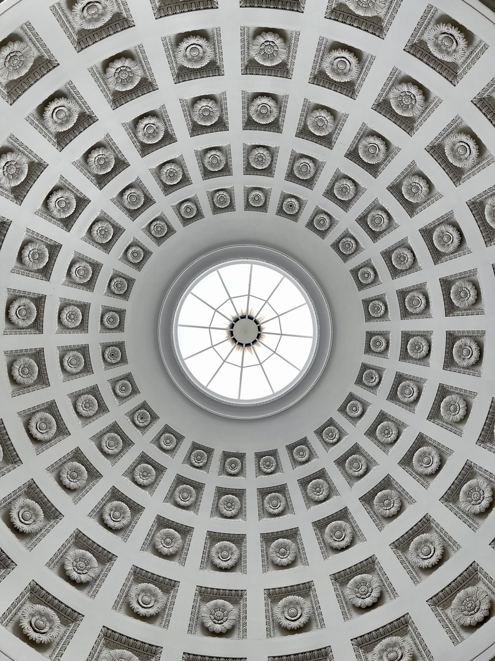 A domed ceiling features a central skylight surrounded by an intricate pattern of square, recessed panels with decorative elements.