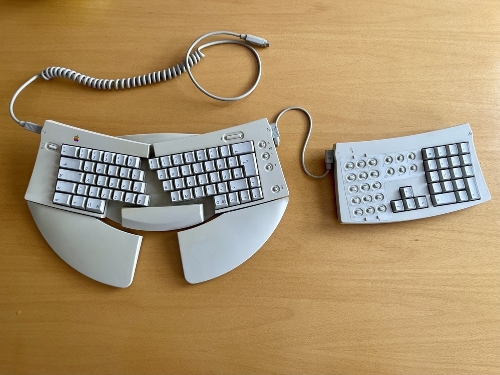 An Apple Adjusrable Keyboard. Asplit ergonomic keyboard with a detached numeric keypad lies on a wooden surface.