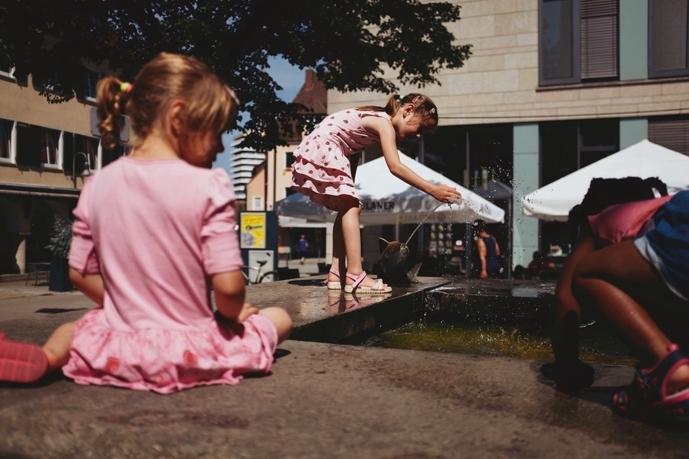 Three small children playing with water at a public city fountain on a hot summer day