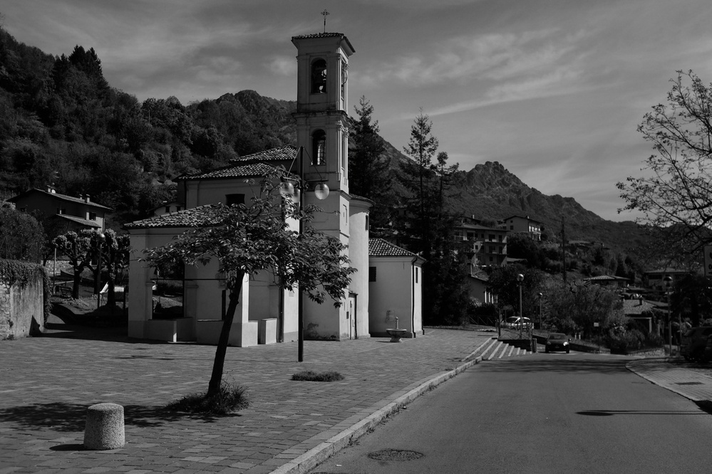 Black-and-white photo of a small village scene with a church in the foreground and mountains in the background