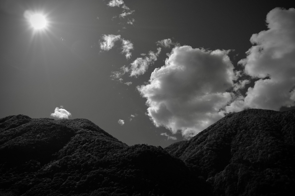 Black-and-white photo of mountain hilltops, clouds and sun