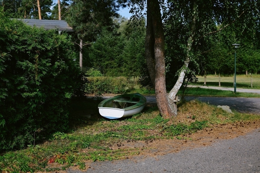 A serene green space with trees, a winding path, and a boat resting peacefully on the grass.