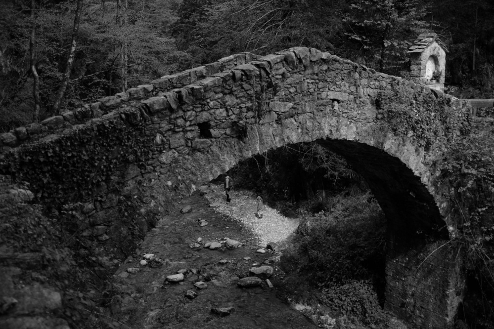 Black-and-white photo of an old stone bridge over a flowing stream