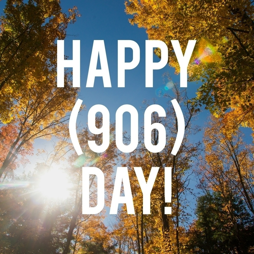 Auto-generated description: Sunlight filters through vibrant autumn trees with the text HAPPY (906) DAY! displayed prominently.