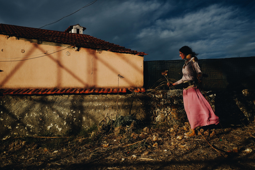 A girl holding a couple of flowers at sunset, close to a house. 