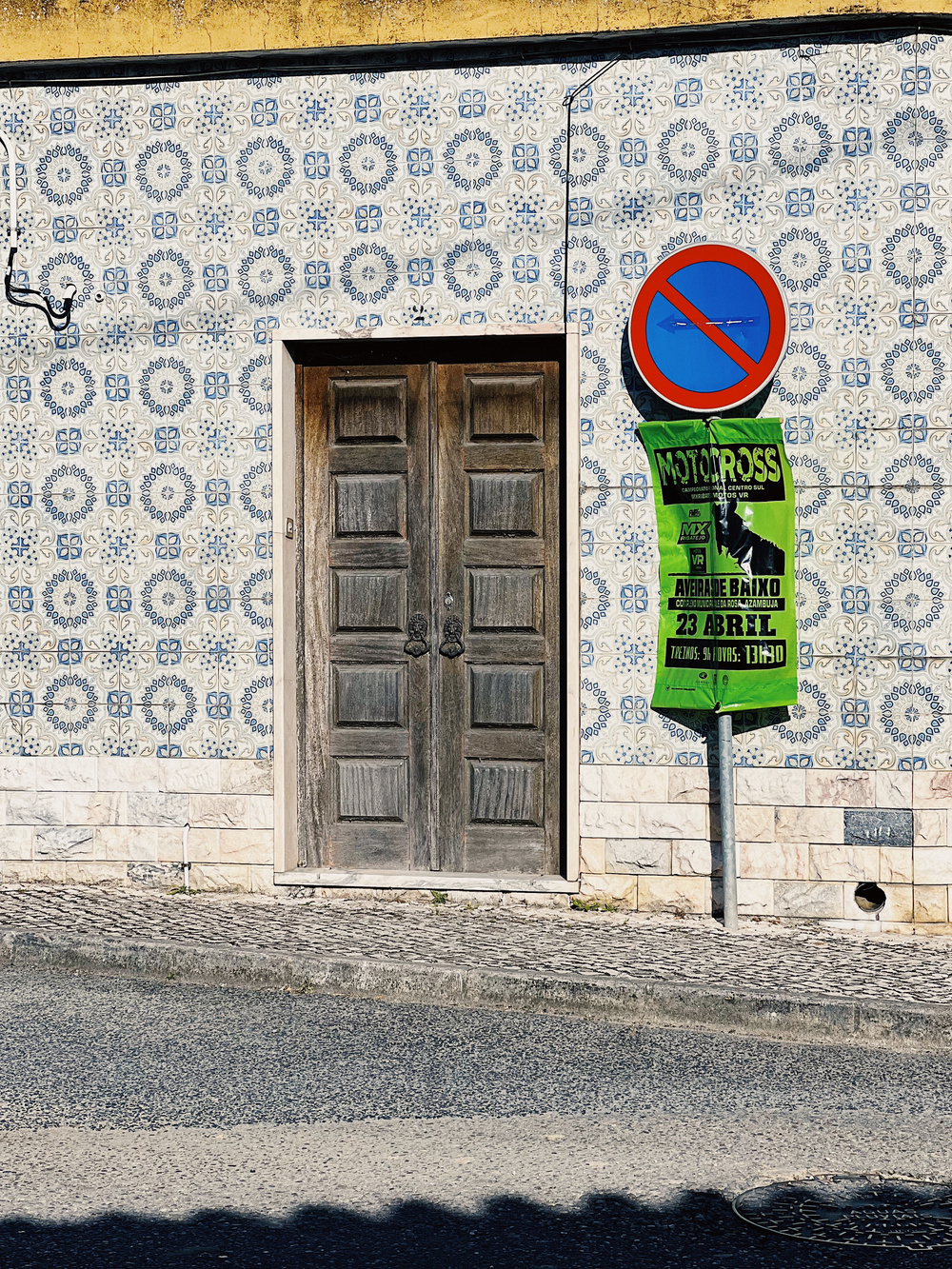 A tiled wall with a wooden door. Street sign next to it. 