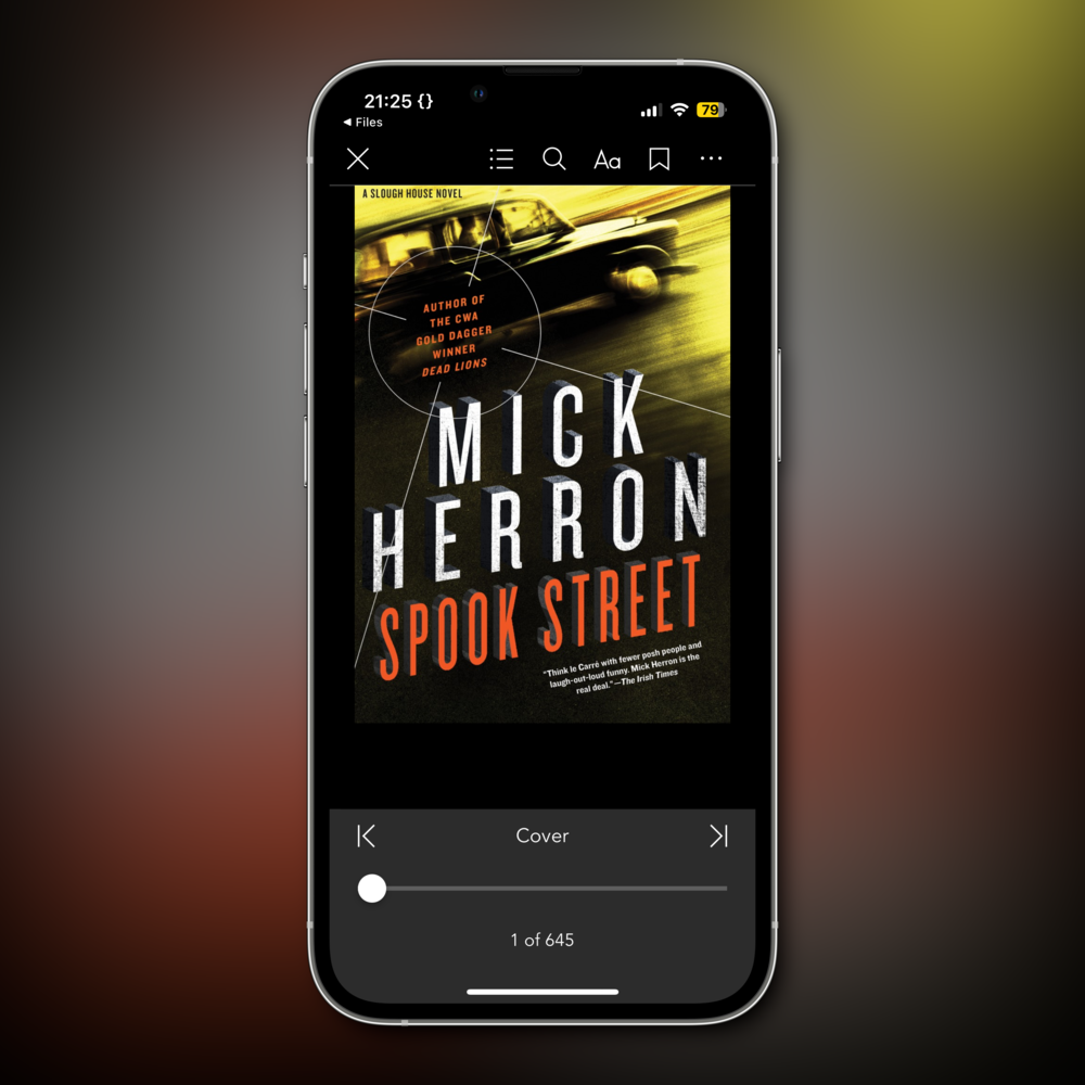 An ebook cover displayed on a smartphone screen. The book title is &ldquo;Spook Street&rdquo; by Mick Herron. The background features a blurred image of a car in motion, and targeting crosshairs.