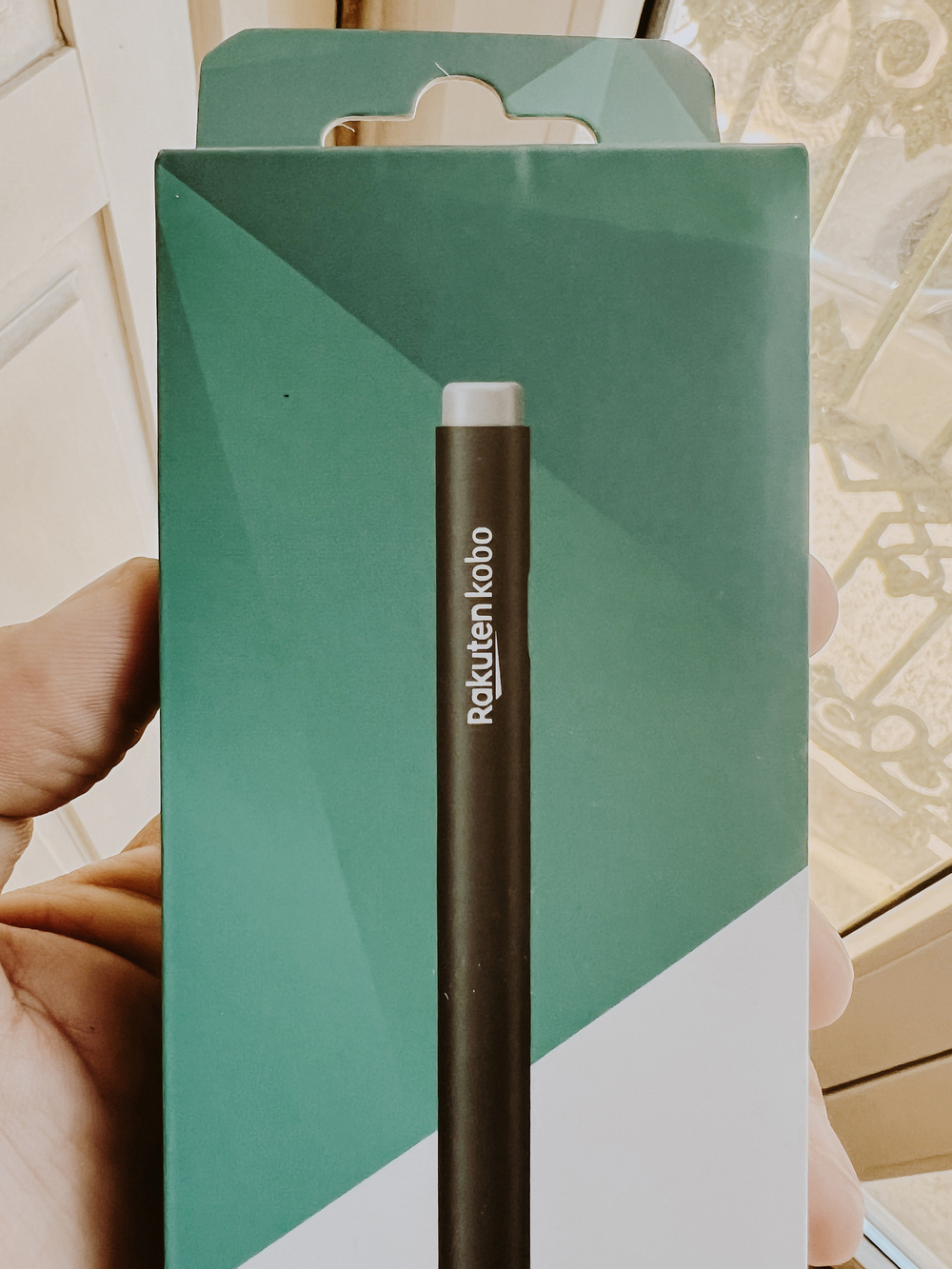 A hand holding a package of a stylus with a green and white background.