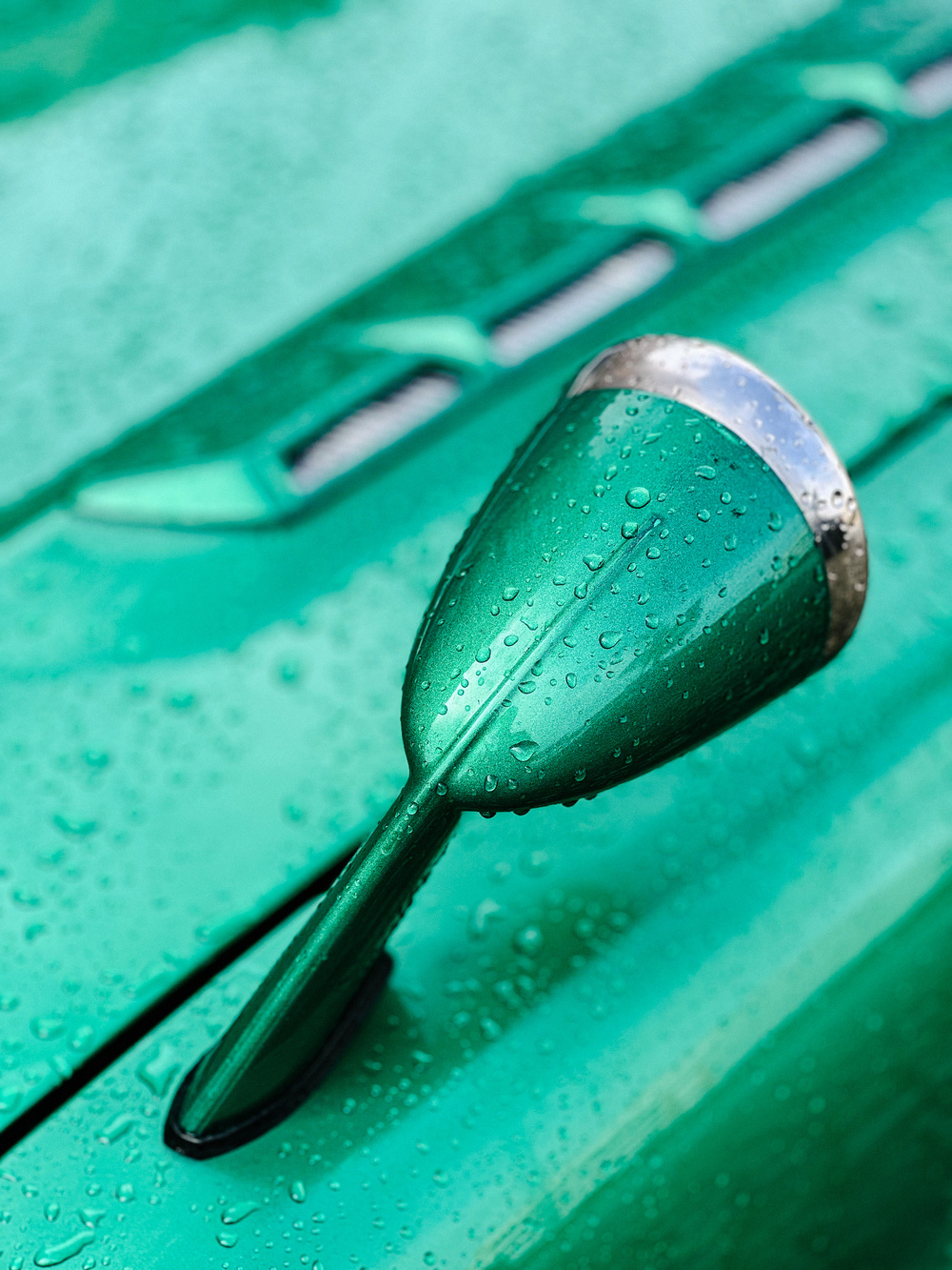 A close-up of a green car&rsquo;s side-view mirror with water droplets on it.