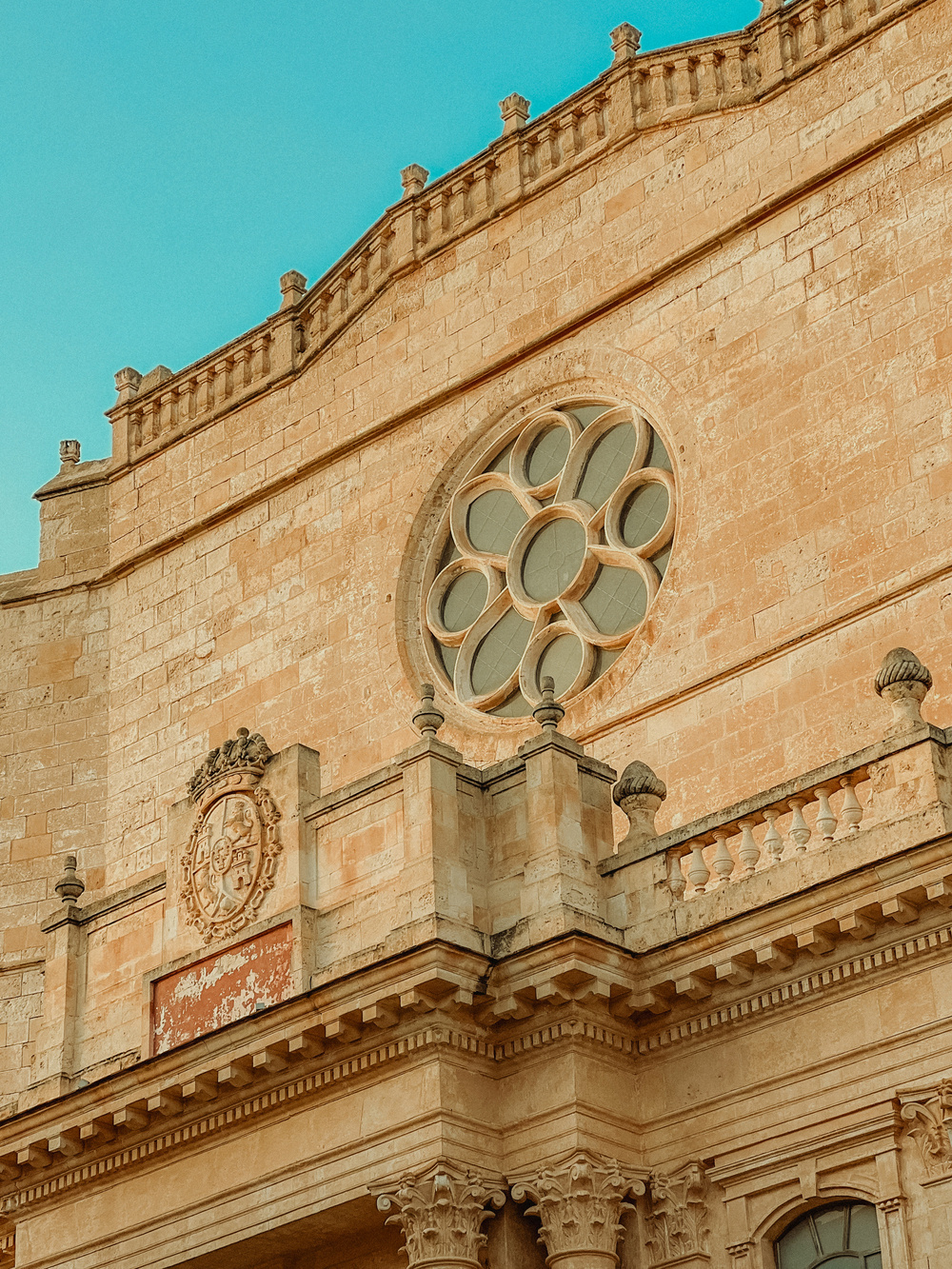 Exterior view of a historical stone building facade featuring a circular rose window and intricate architectural details against a clear blue sky.