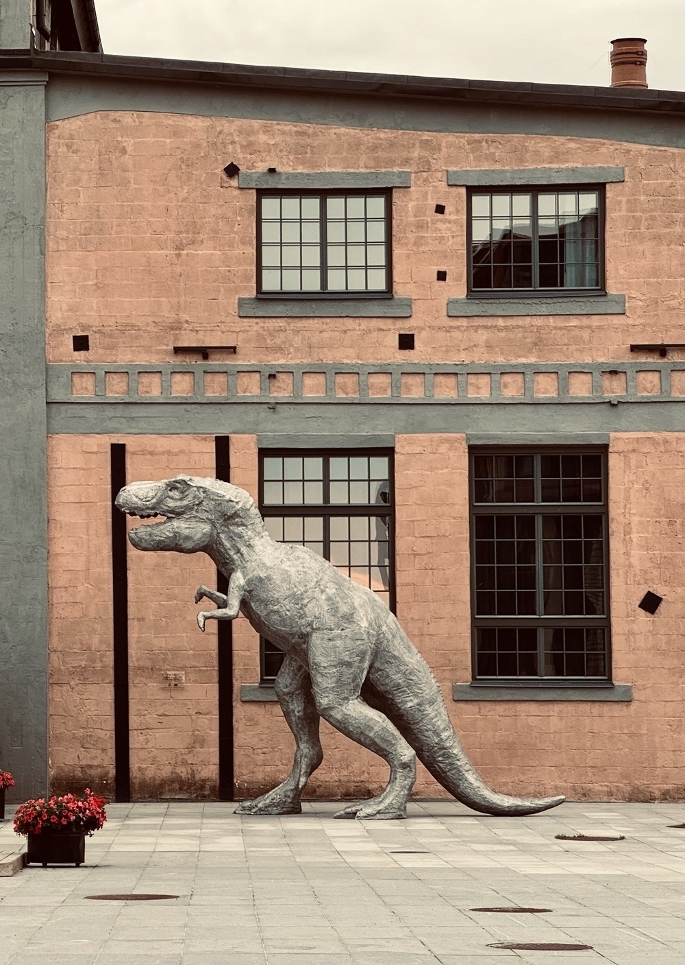 A statue of a Tyrannosaurus Rex in front of an orange and grey building.