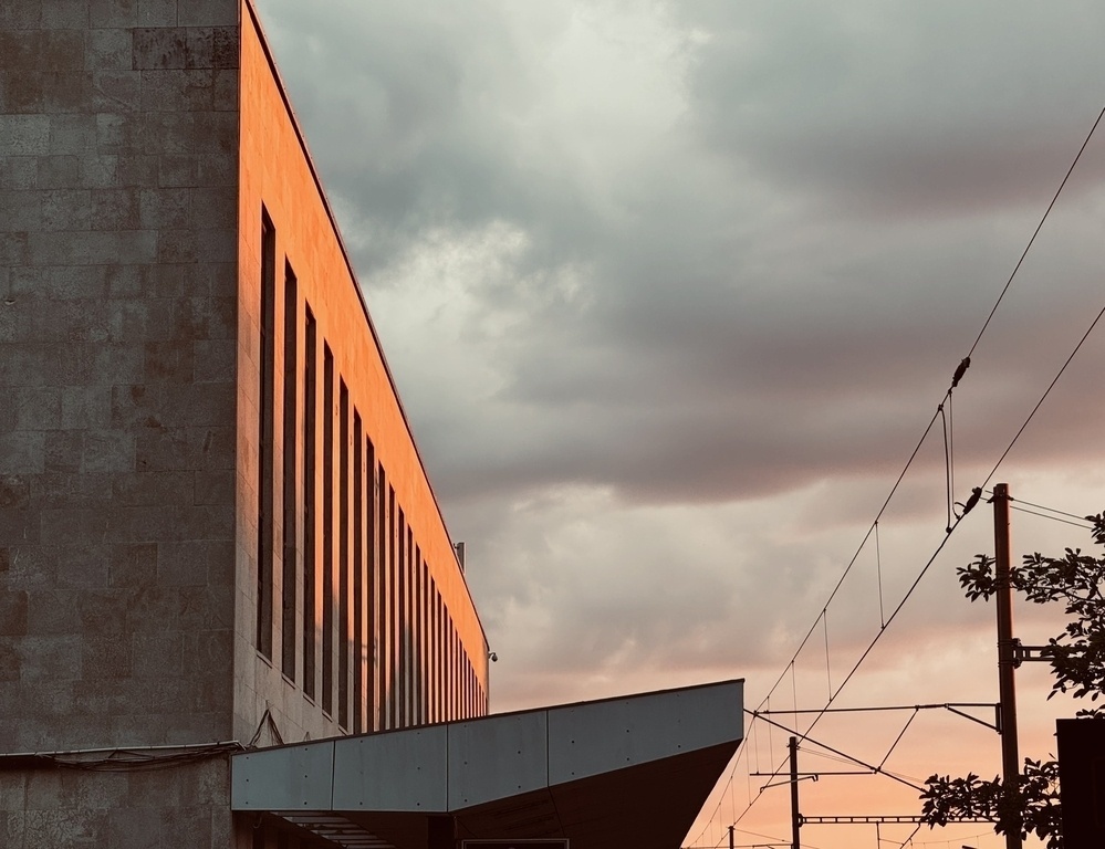 The stone facade of a train station glowing orange in the light of the setting sun.