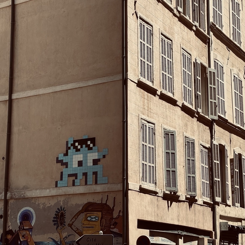 Pixel art on the shady side of a building, with the other face of the building in the sunlight.