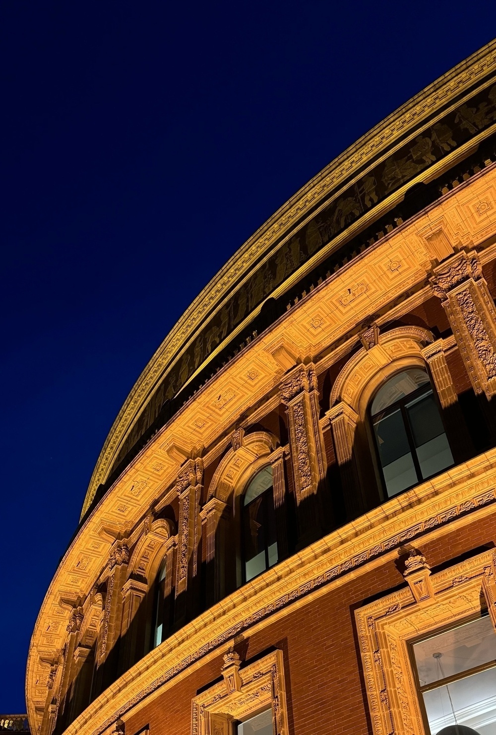 The lit facade of the Royal Albert Hall curving against a deep blue night sky.
