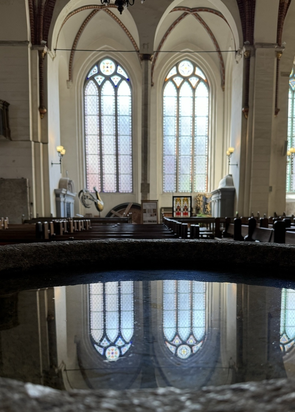 Arched windows in a church reflected in the water of a font.