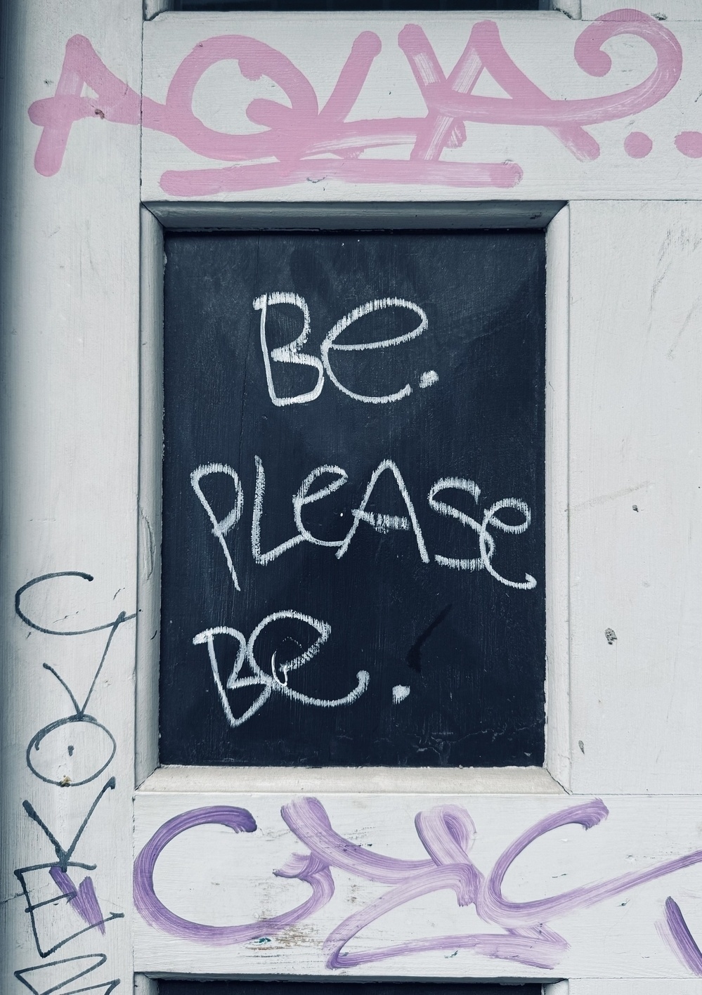 Graffiti on a door that says “Be. Please be.”.