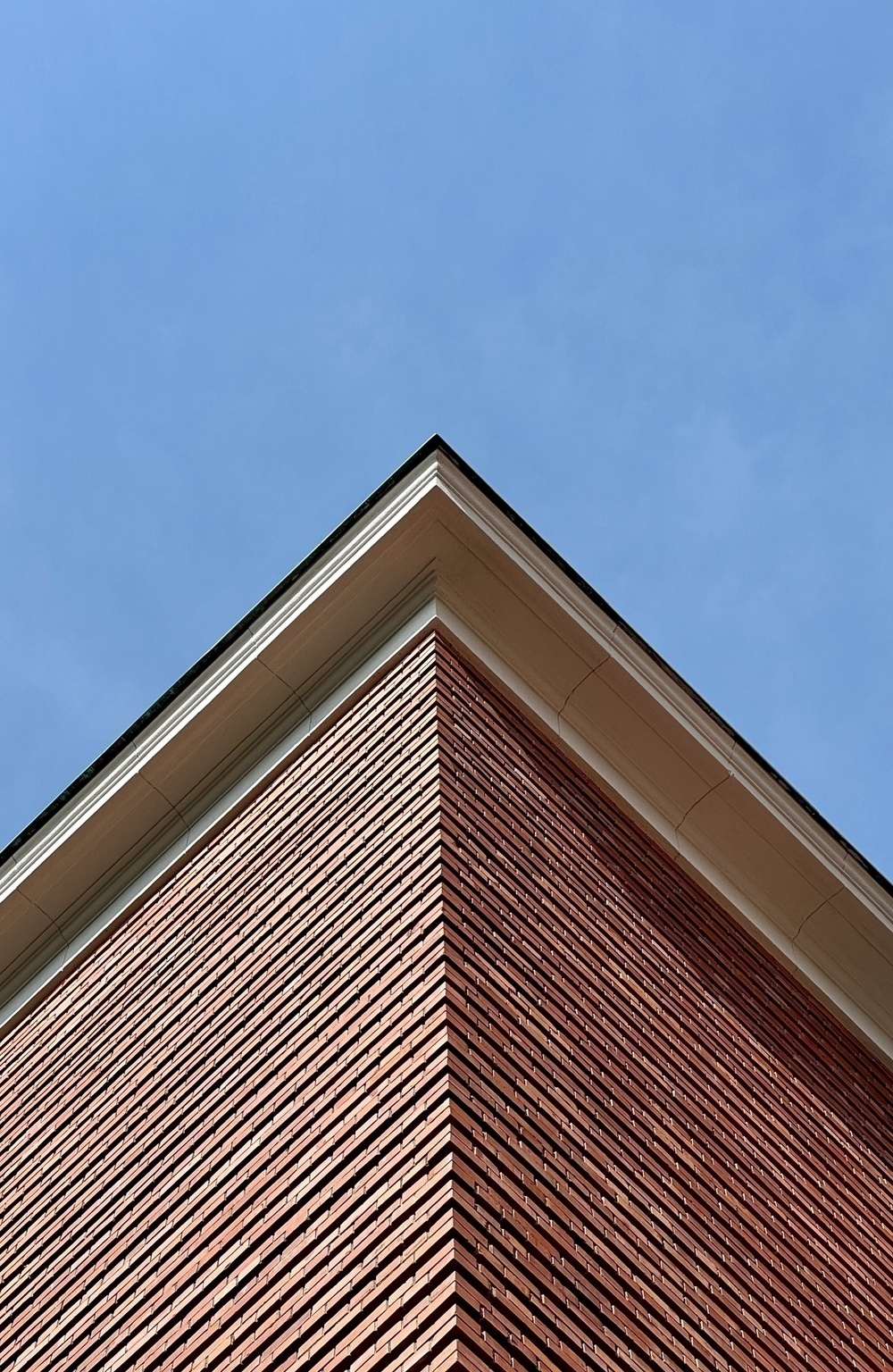 The sharp brick edge of a building running up the middle of the photo to a blue sky.