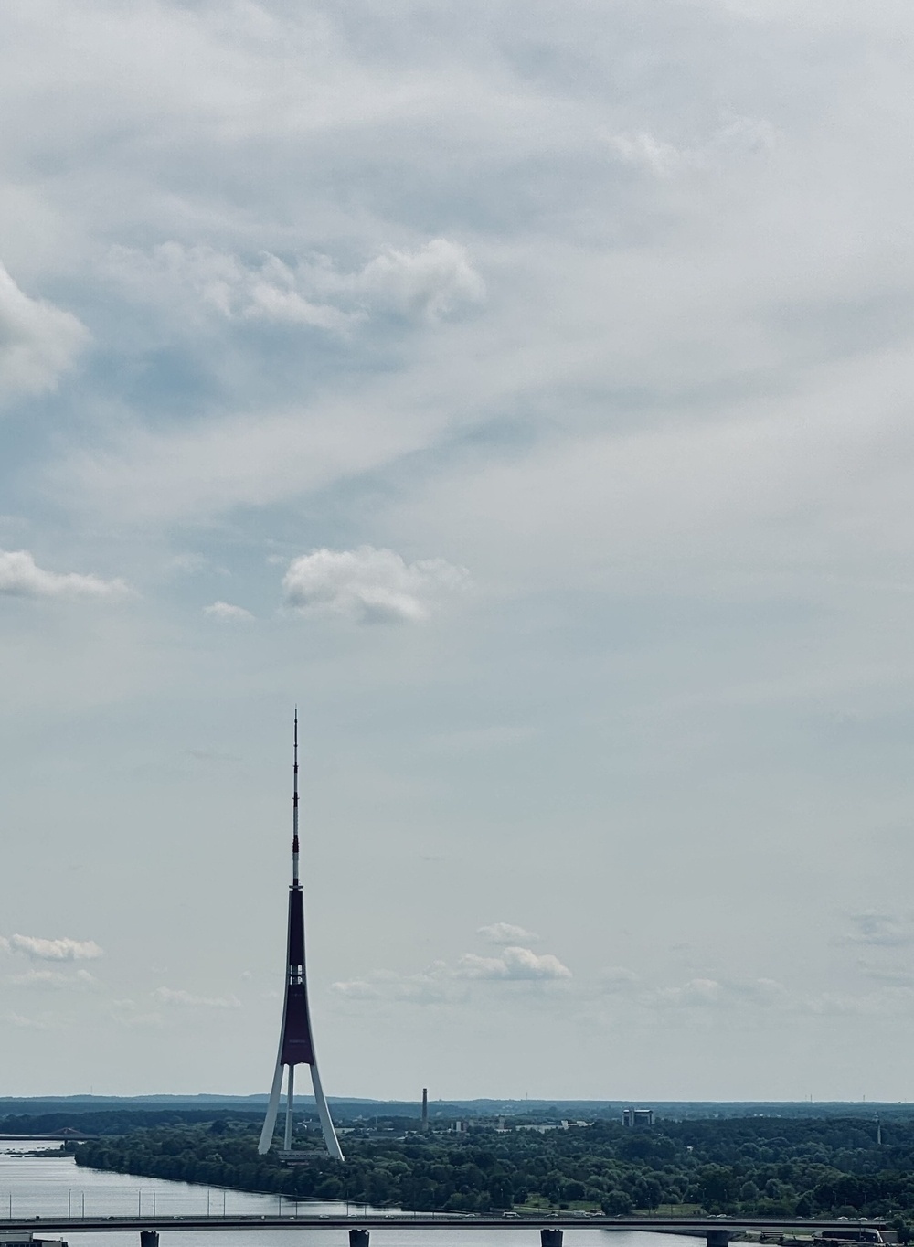 The tripod like transmission tower in Riga, seen from a distance against a cloudy sky.