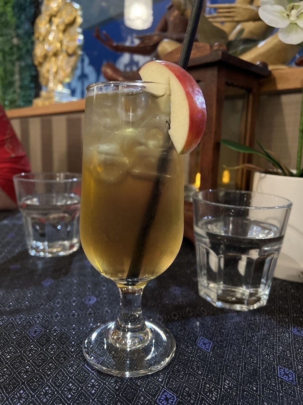 A glass of applejuice, with a straw and a slice of apple. 