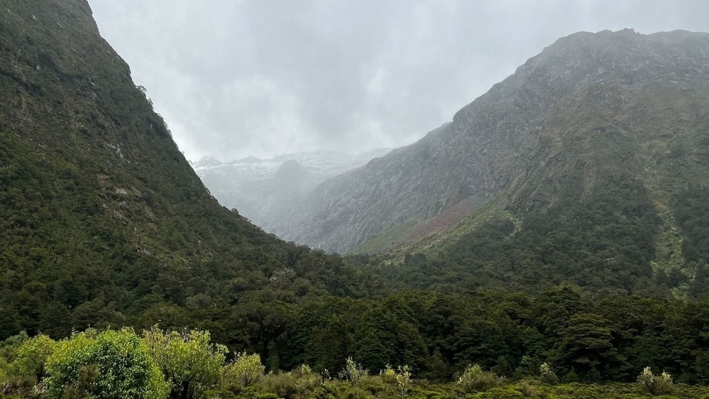 View through a misty valley to snow-topped mountains beyond. 