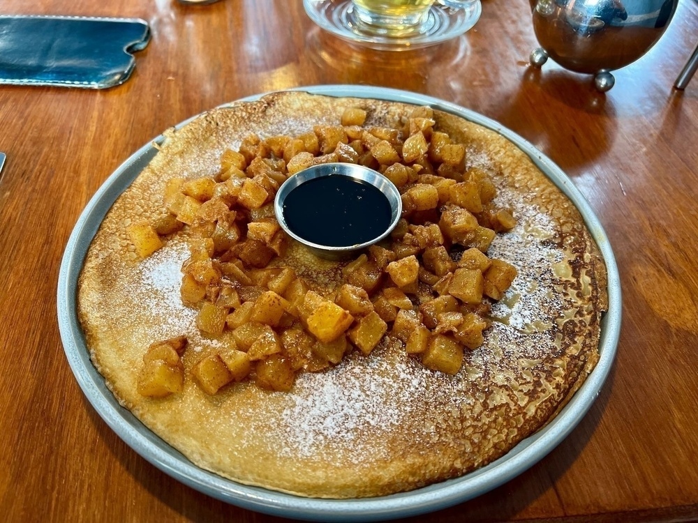Dutch pancake with cubes of spiced apple on top and a small bowl of syrup. 
