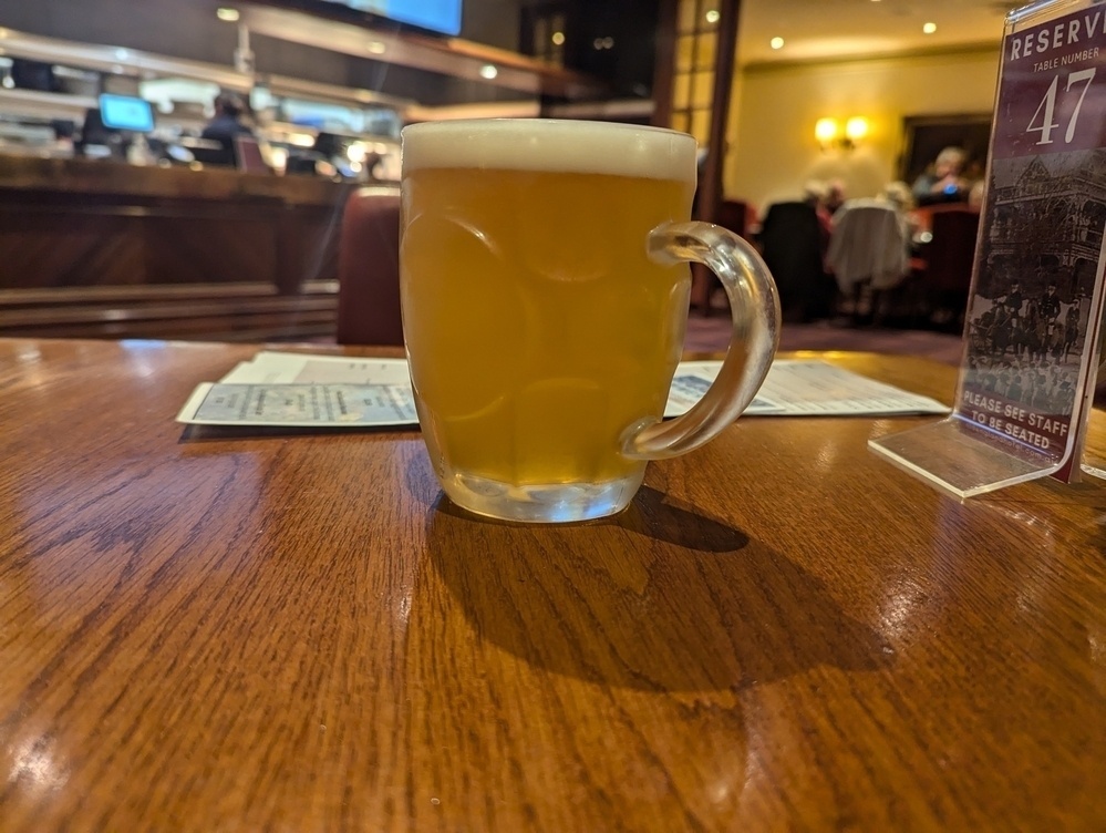 A frothy mug of beer sits on a wooden table in a cozy restaurant setting.