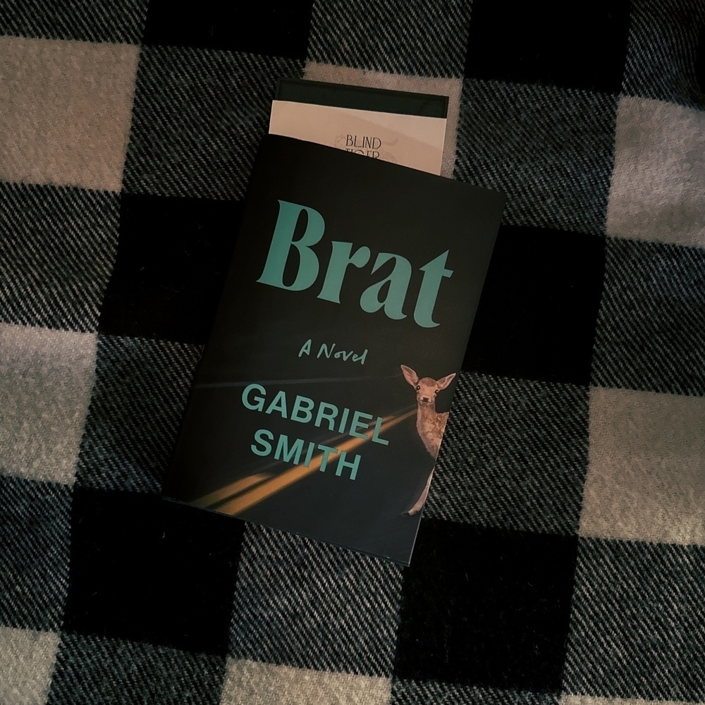 Book Calle Brat with blue text and deer in headlight on cover resting on plaid black and white blanket