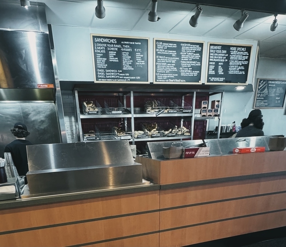 Interior of a bagel shop with rows of baked goods and menus on chalkboards above