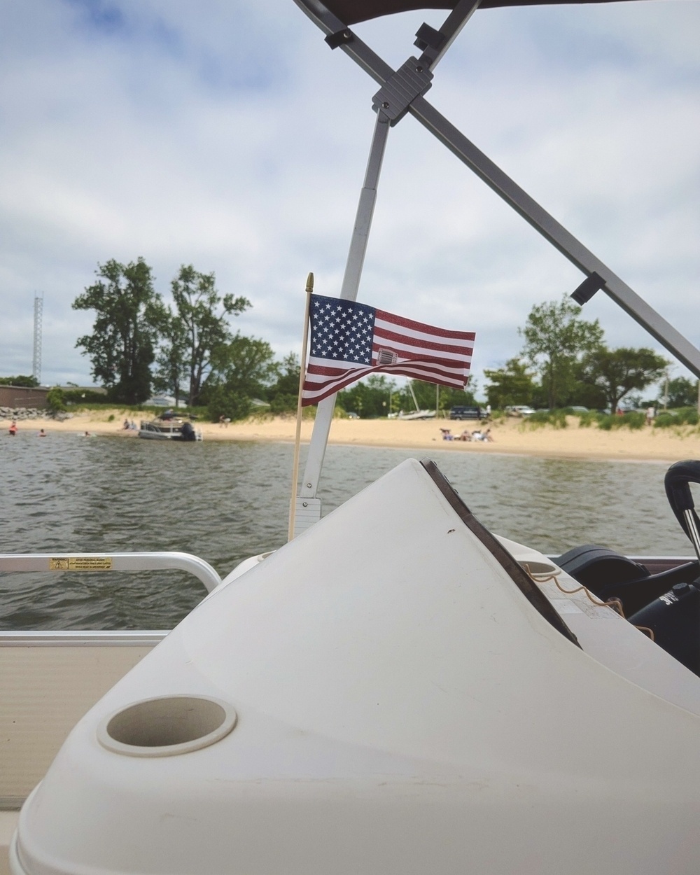 a USA flag in the wind atop a pontoon boat cockpit with a sandy beach in the background