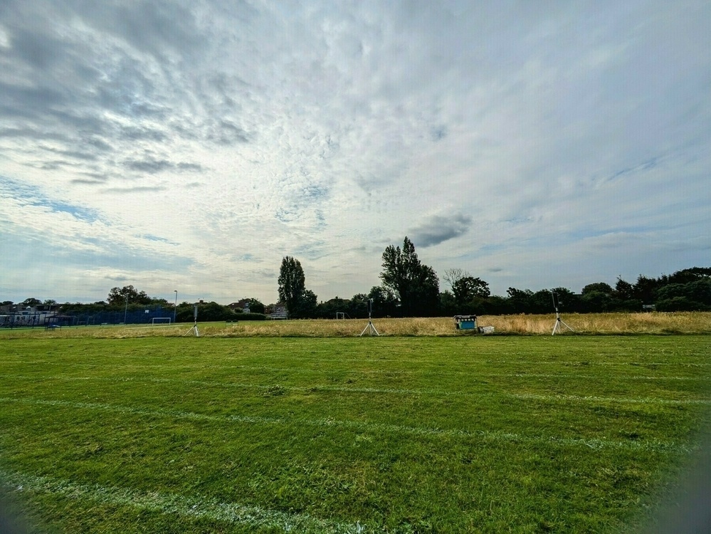 Wide angle photo of school sports day white lined running lanes in the foreground, with uncut meadow in the background 