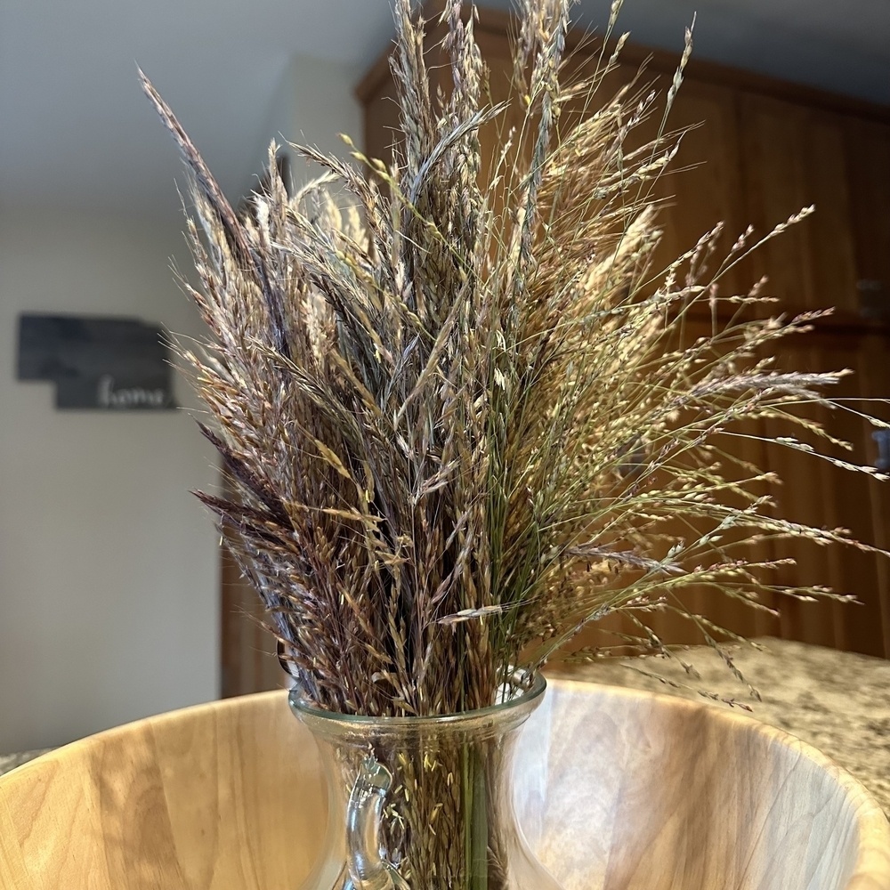 A collection of prairie grasses in a glass vase sitting in a wooden bowl. 