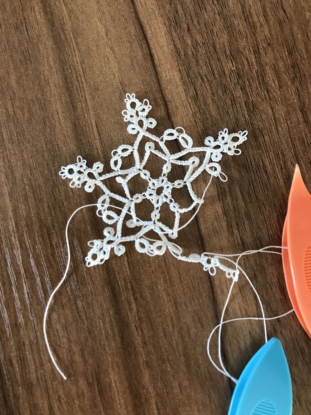 half-finished tatted white snowflake on a desk, with the shuttles still attached”></p>
