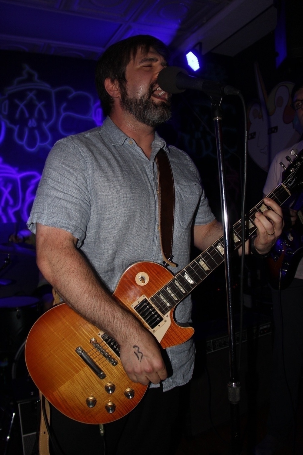A bearded musician (me) joyfully plays an electric guitar (Les Paul) and sings into a microphone on stage.