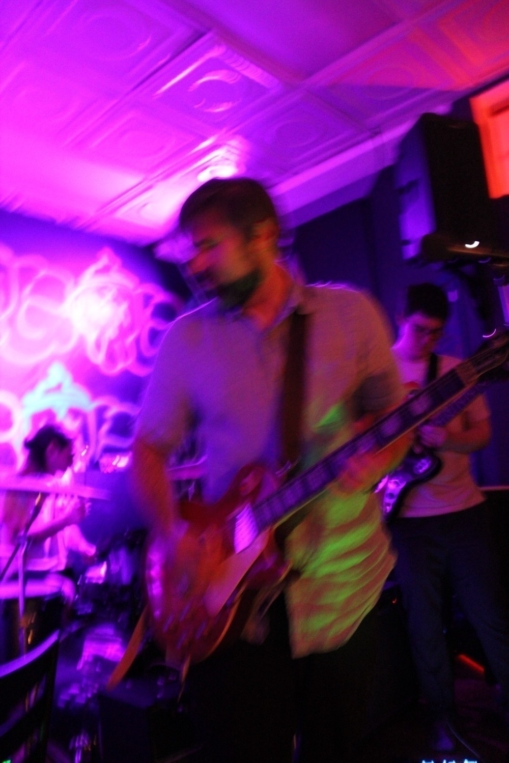 A band (Ancestral Worm) is performing on stage under vibrant purple and pink lighting.