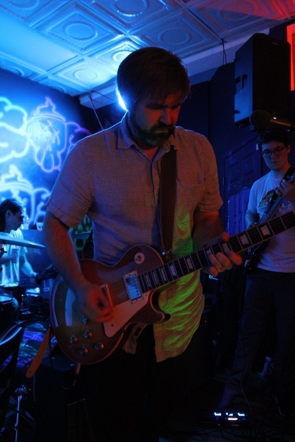 A musician (me) is playing an electric guitar (Les Paul) in a dimly lit room with neon wall art.