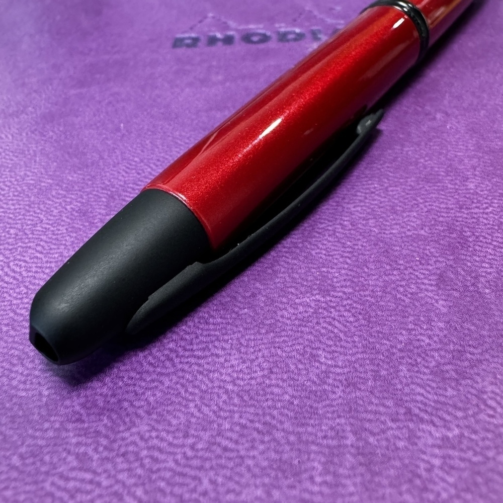 A red pen with a black cap and clip rests on a purple surface.