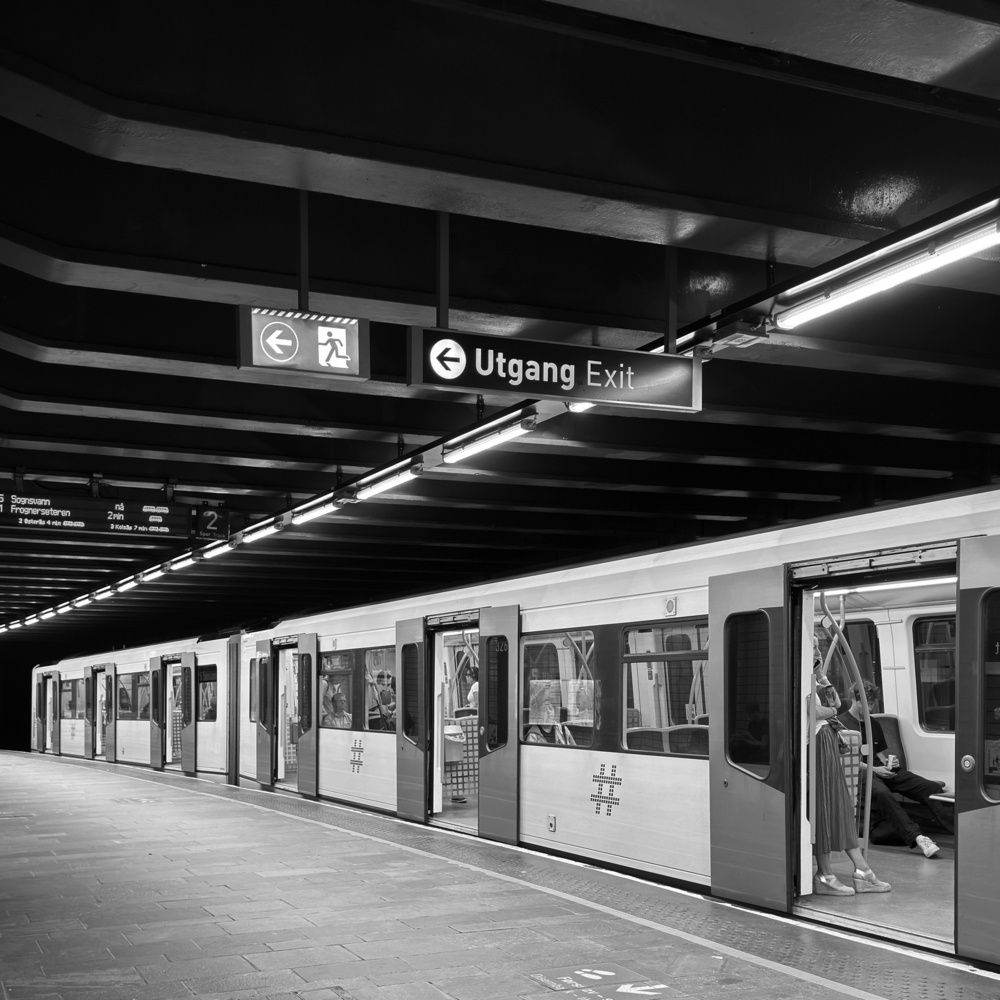 A subway train is stopped at a station platform with open doors and exit signs overhead.