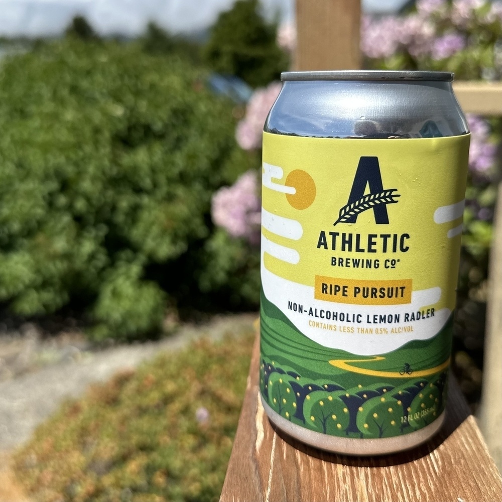 Can of beer with yellow-green design, sitting on porche, flowers and clouds in the background 