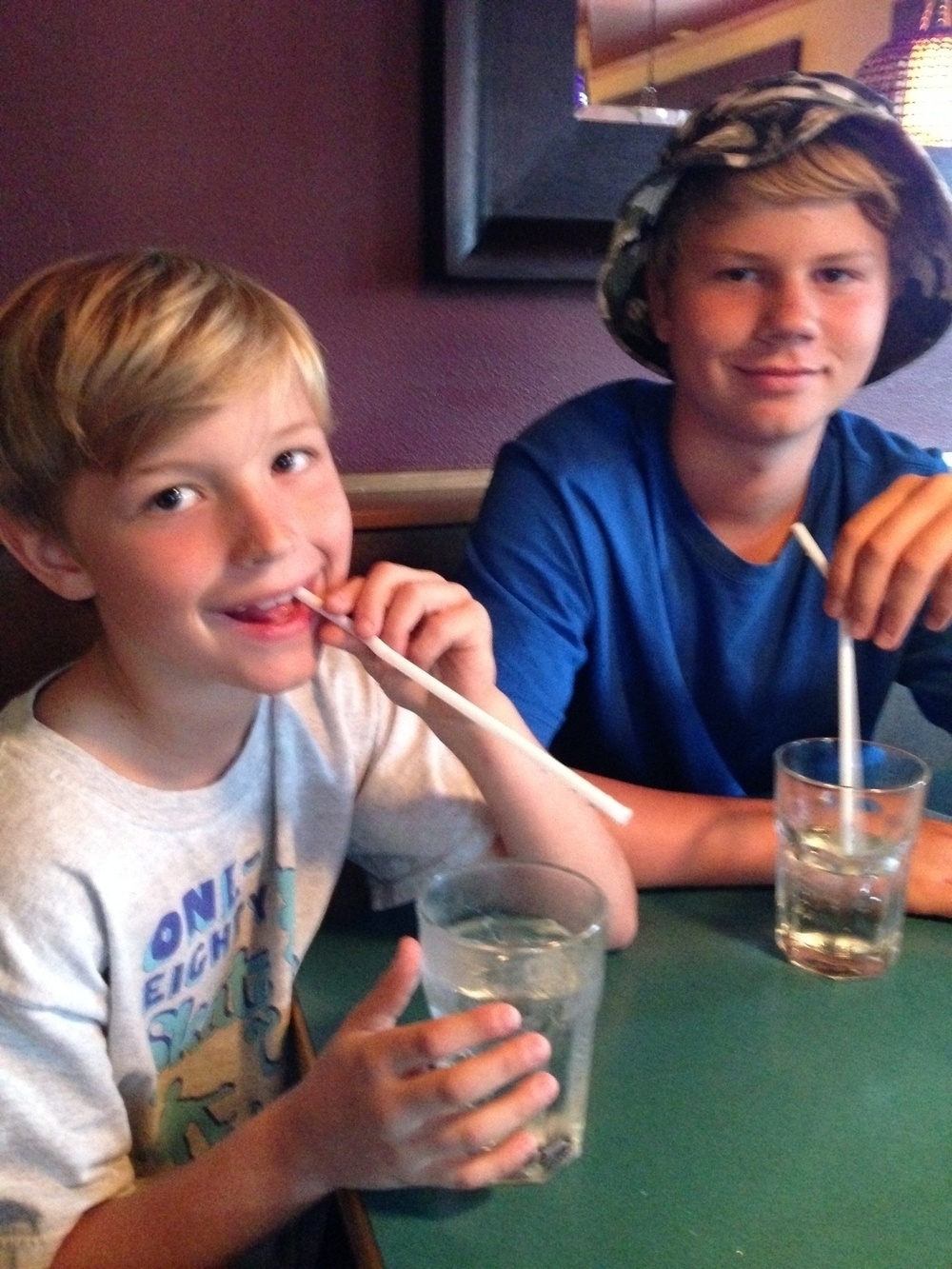 Two boys drinking soda at a table. 