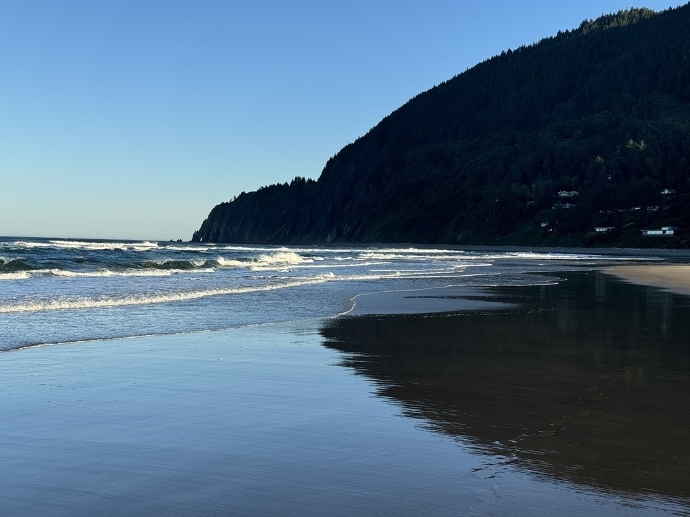 Coastal mountain, clear blue sky background, white waves crests in the foreground. 