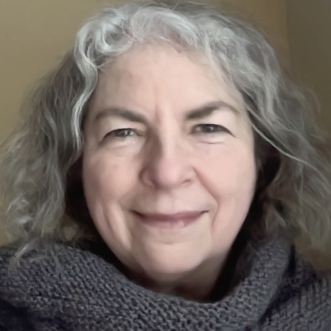 woman with white/brown curly hair smiling, knitted wrap on her shoulders