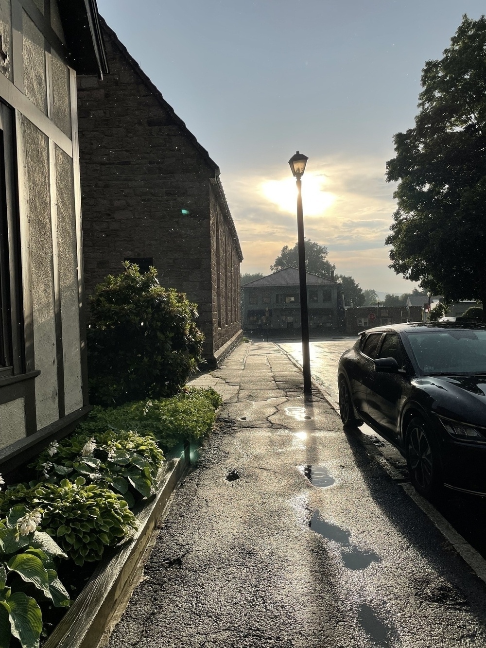 Sidewalk with rain, sun, lamppost, and parked car