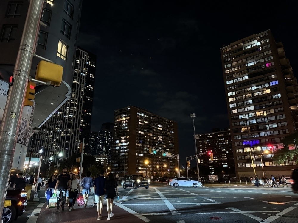 A street view of the Jersey city skyline at night. It’s very busy on the streets. 