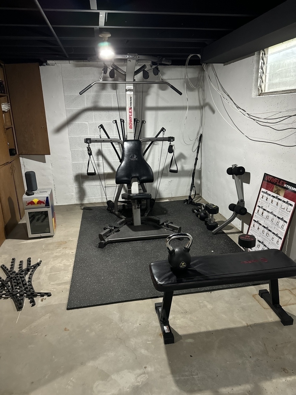 An old Bowflex set up in my basement along with a bench and various kettle bells and dumbbells. 