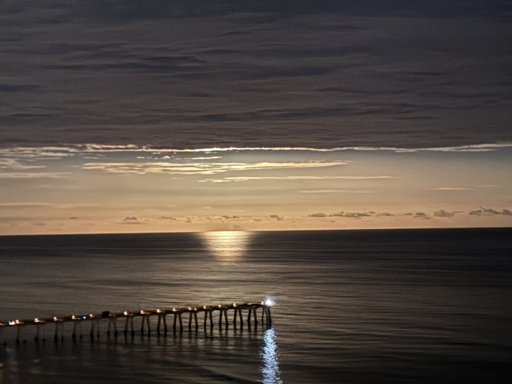 Navarre beach at moon rise. The moon is risen above the clouds and is not visible. Below the ocean is seen reflecting the moons light. Due to the hidden moon it appears the ocean is lit up with no light source at all. 