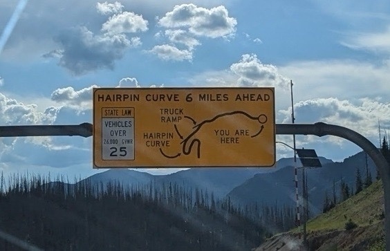 A road sign that says “HARPIN CURVE 6 MILES AHEAD” with a diagram of the hairpin layout.