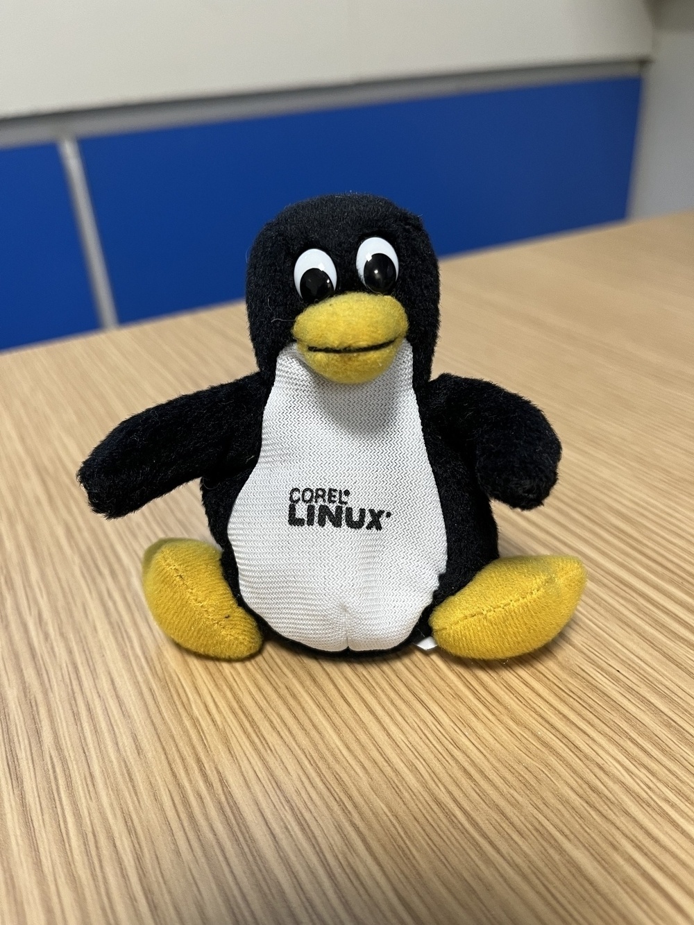 A small beanbag stuffed penguin toy sitting of a desk, with “Corel Linux” printed on its chest. 