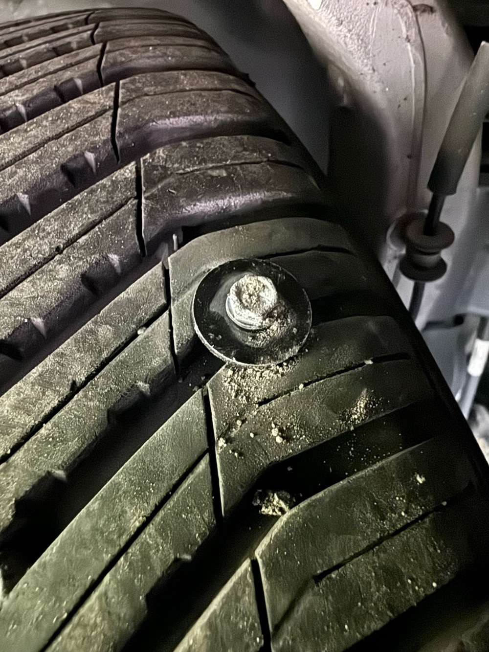 An image of a metal screw with a washer embedded into the tread of a car tire.