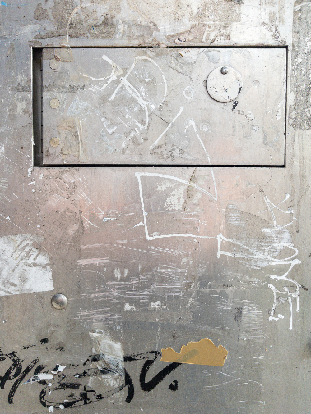 Picture of a metal plate with a hinged rectangular access panel at the top, slightly off center, and faded graffiti. 
