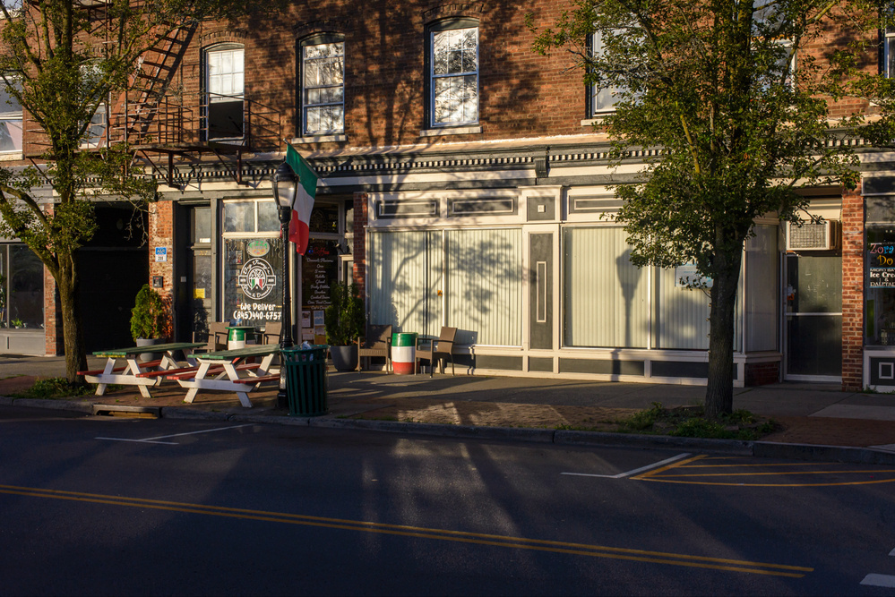 Commercial street scene with early morning sun illumination of storefront and picnic tables.